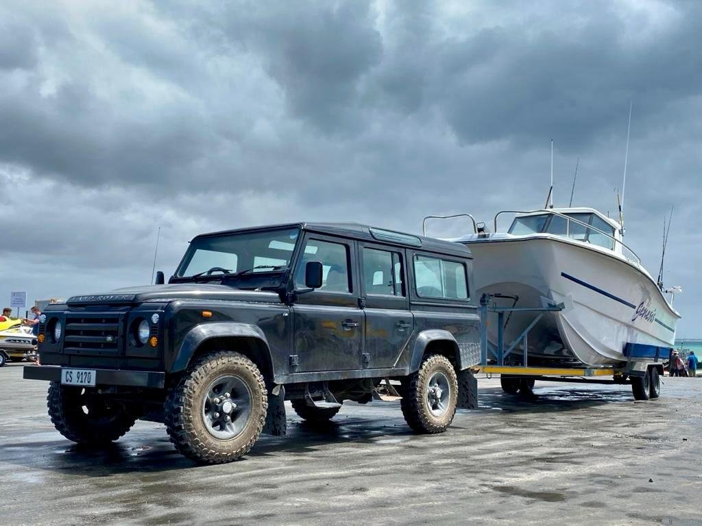A black off-road vehicle towing a boat on a trailer on a wet concrete surface with a cloudy sky overhead.