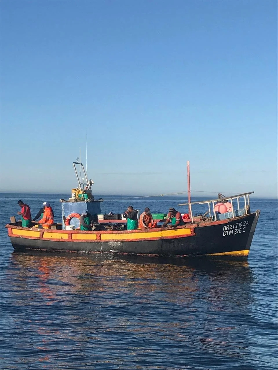 A small fishing boat with several people on board is on calm water under a clear blue sky.
