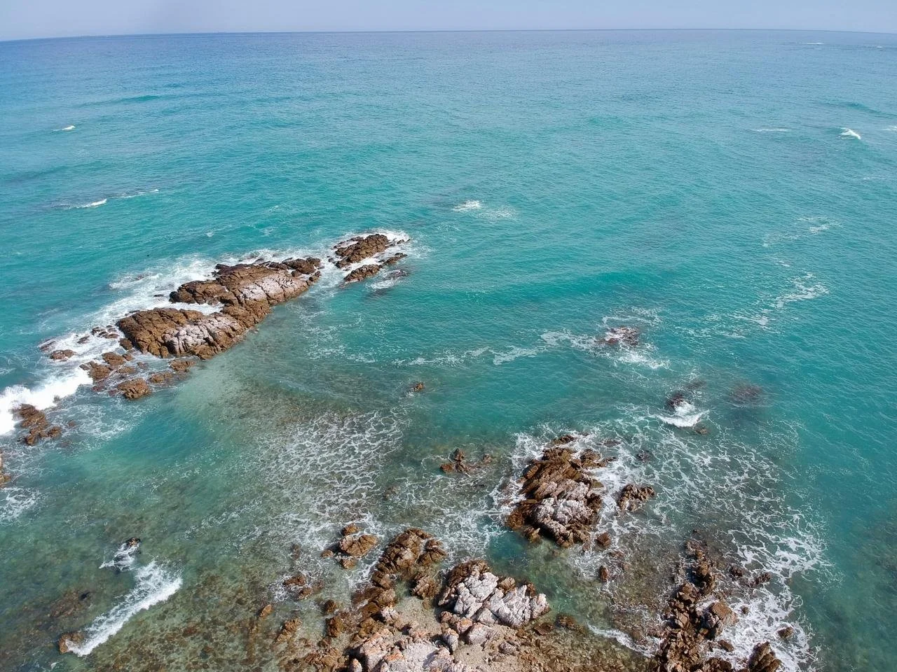 Aerial view of a turquoise ocean with rocks and small waves close to the shore.