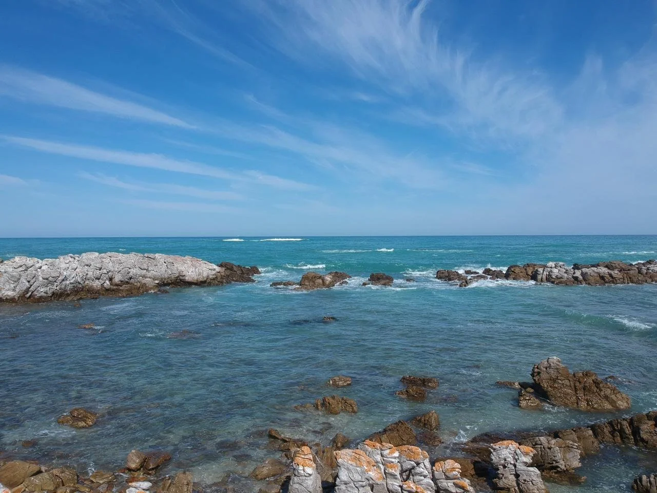 Rocky shoreline with blue ocean and sky with wispy clouds.