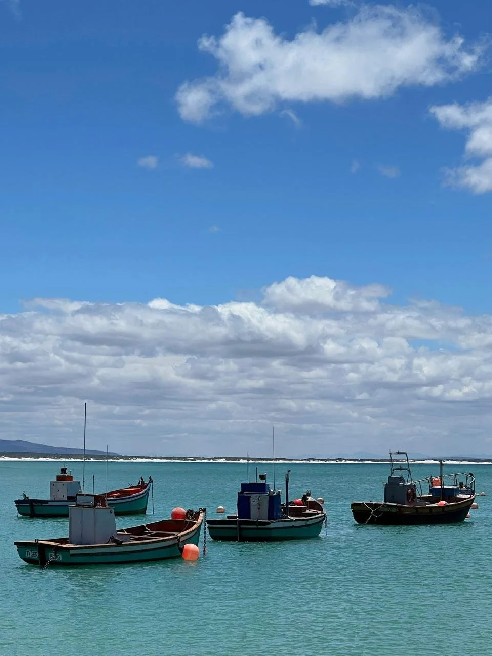 Several small boats floating on calm turquoise water under a partly cloudy sky, with distant land in the background.