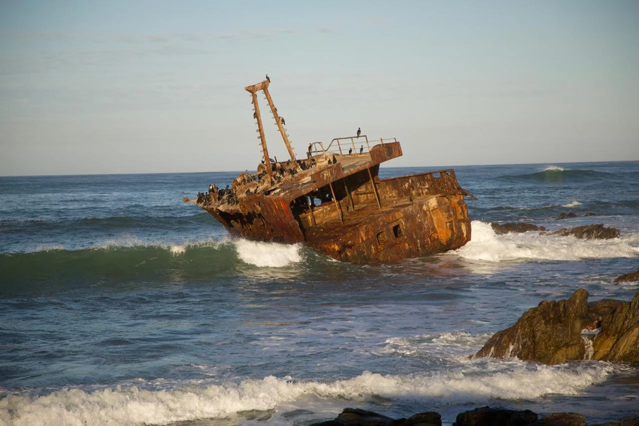 An old, rusted shipwreck partially submerged in the ocean near rocky shoreline