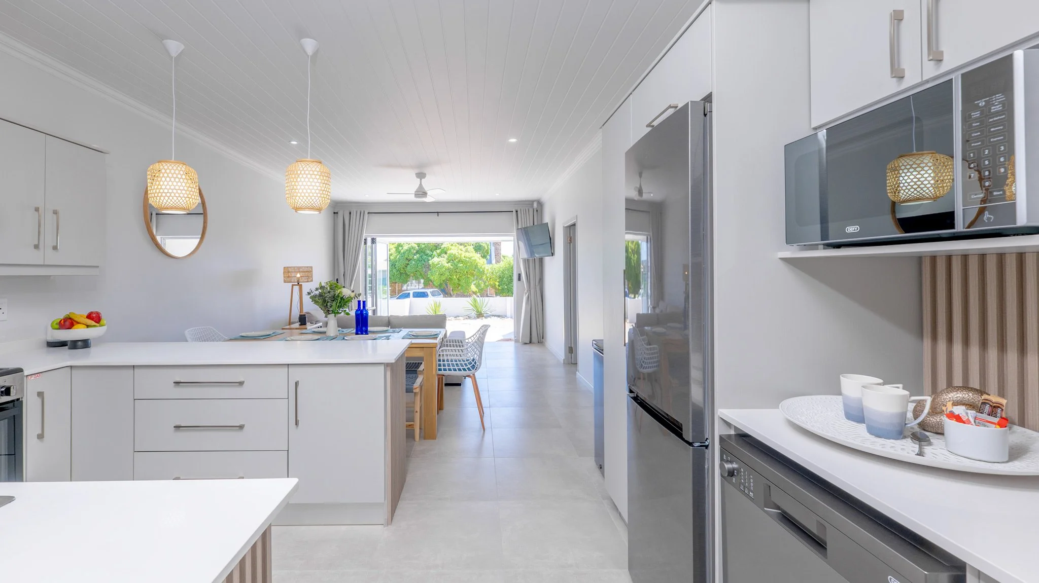 Modern kitchen and dining area with white cabinets, a table set, and a bright living room visible through an open doorway.