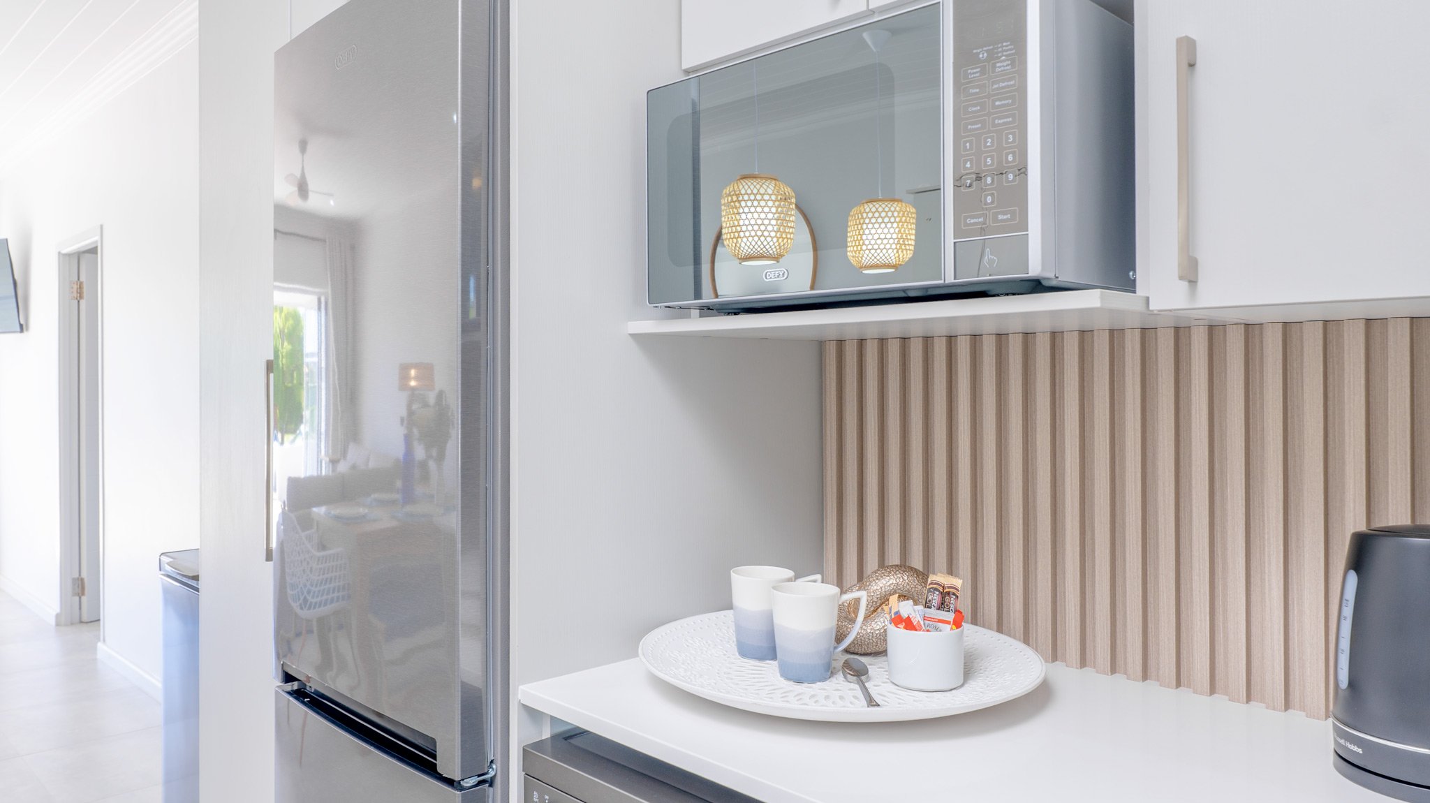 Modern kitchen area with a microwave, fridge, and a white countertop. 