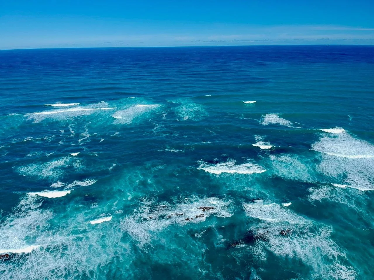 Aerial view of the ocean with waves and a clear blue sky.