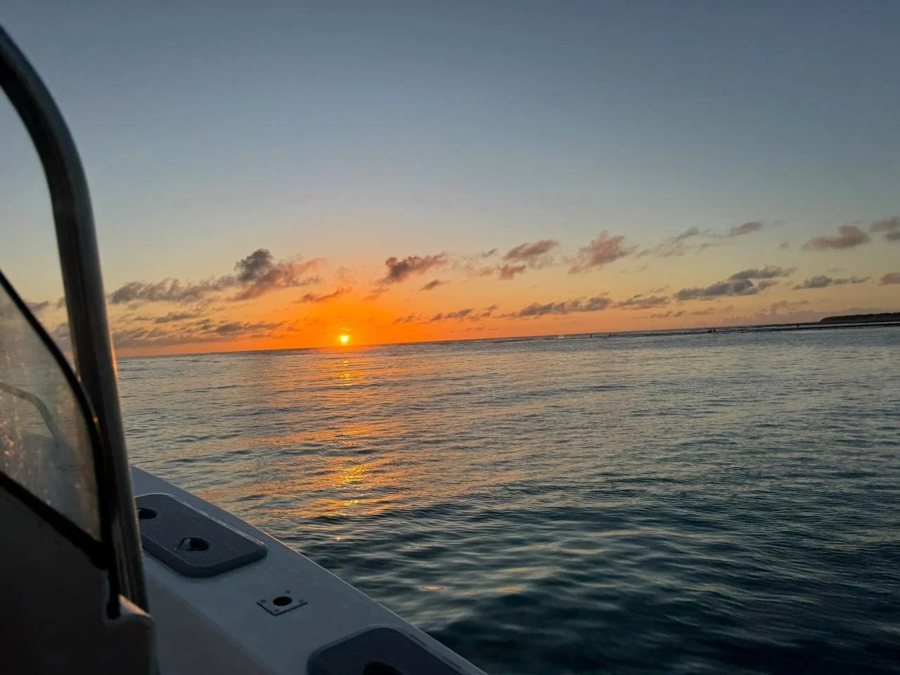 View of a sunset over the ocean taken from a boat, with part of the boat's side visible in the foreground.