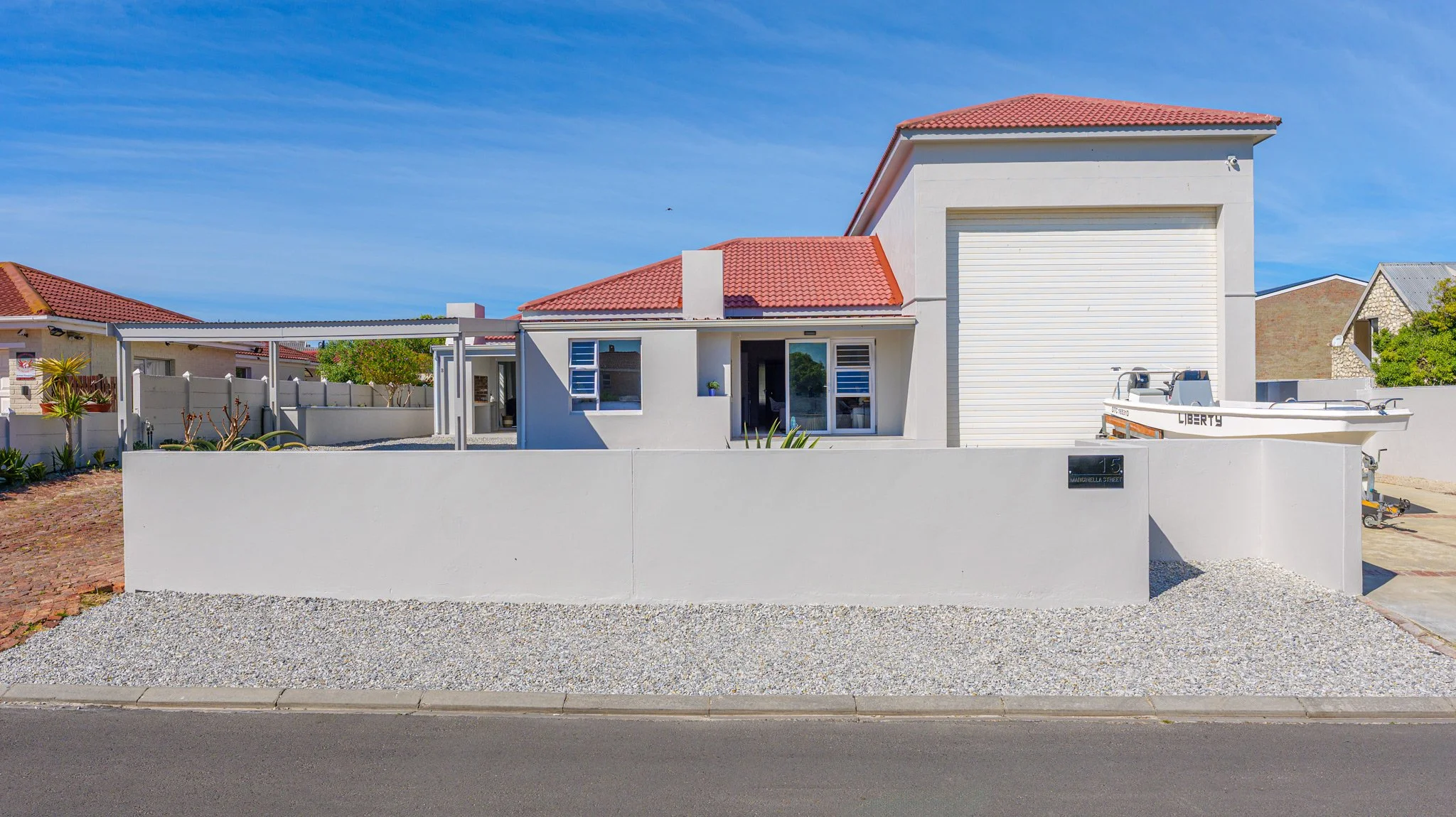 Modern white house with red-tile roof, front yard with gravel, and boat on trailer in driveway
