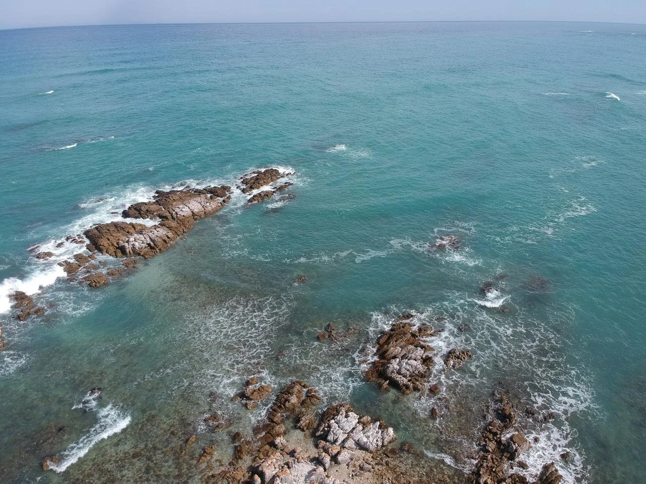 Aerial view of the ocean with rocks and waves near the shoreline