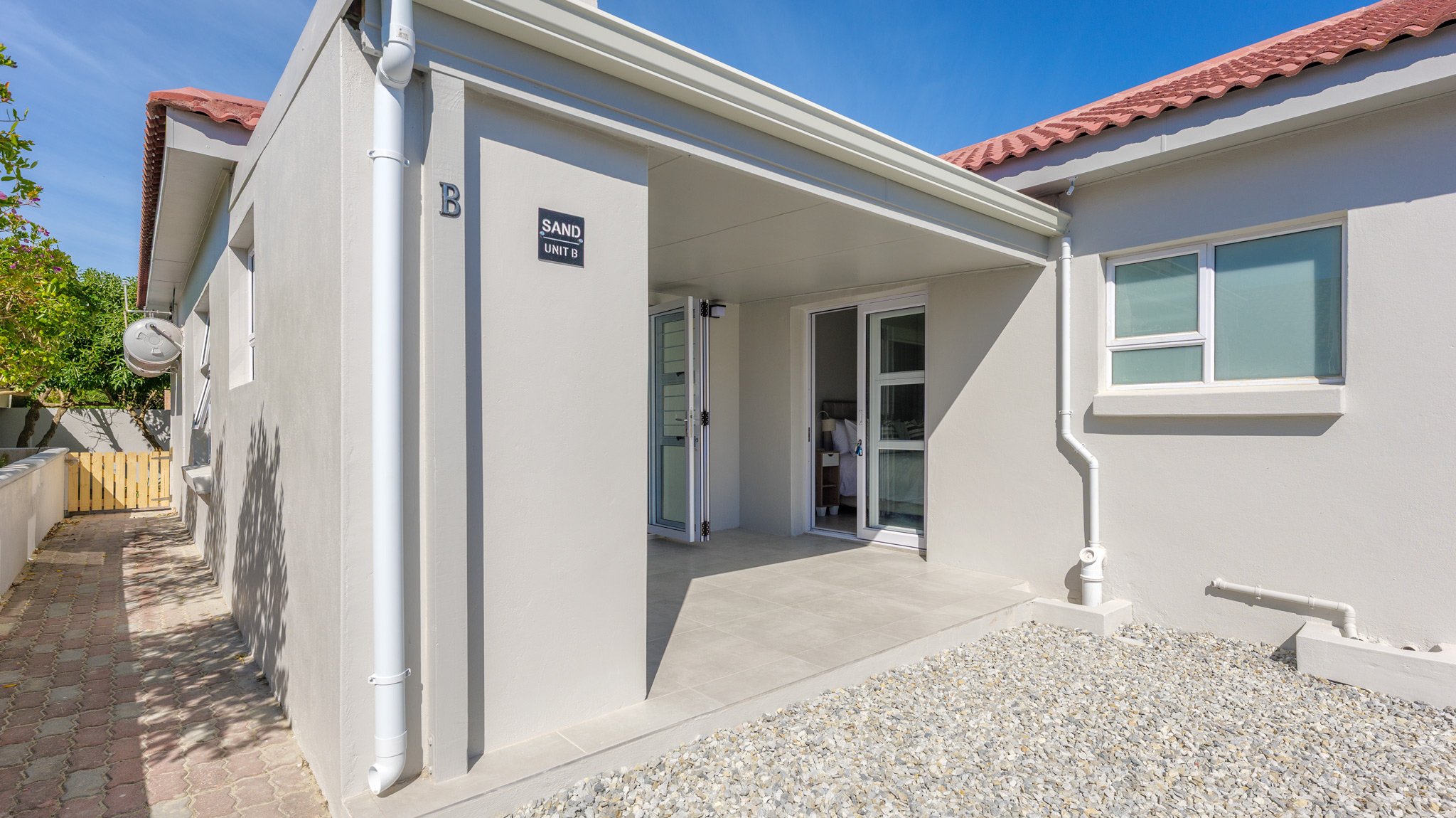 Exterior view of a modern house with a small porch, white walls, a sliding glass door, and a window, under a blue sky with some clouds.
