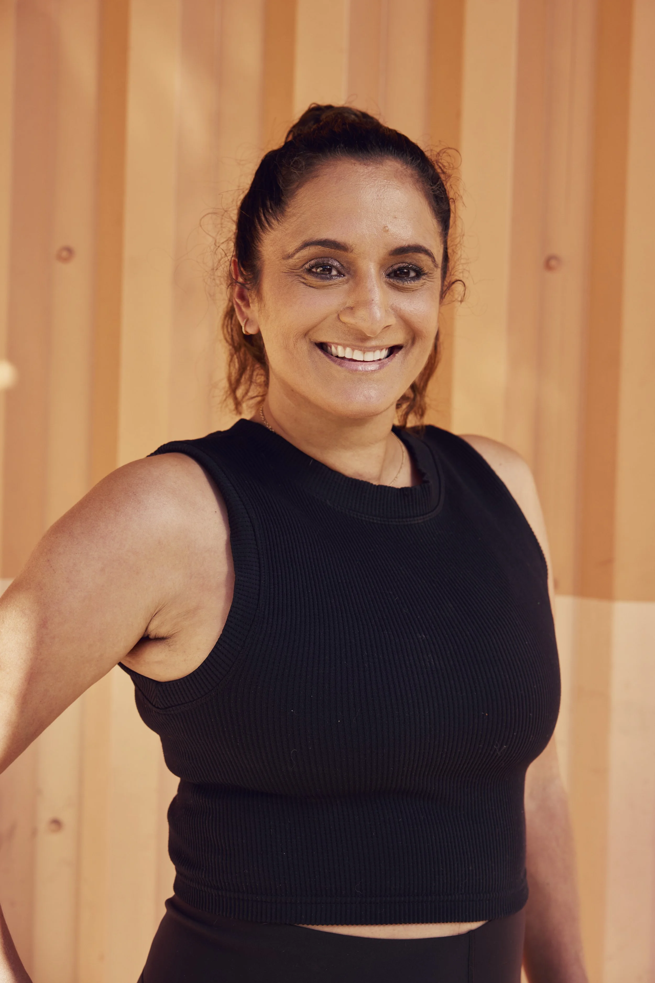 A woman with long brown hair, wearing a black shirt, places her hand on her chest and tilts her head slightly down with a thoughtful expression.