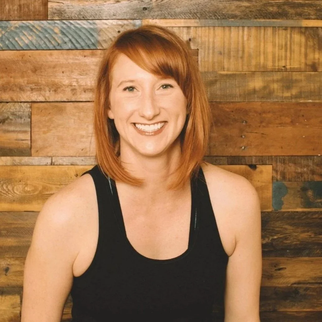 A woman with red hair smiling in front of a wooden wall.