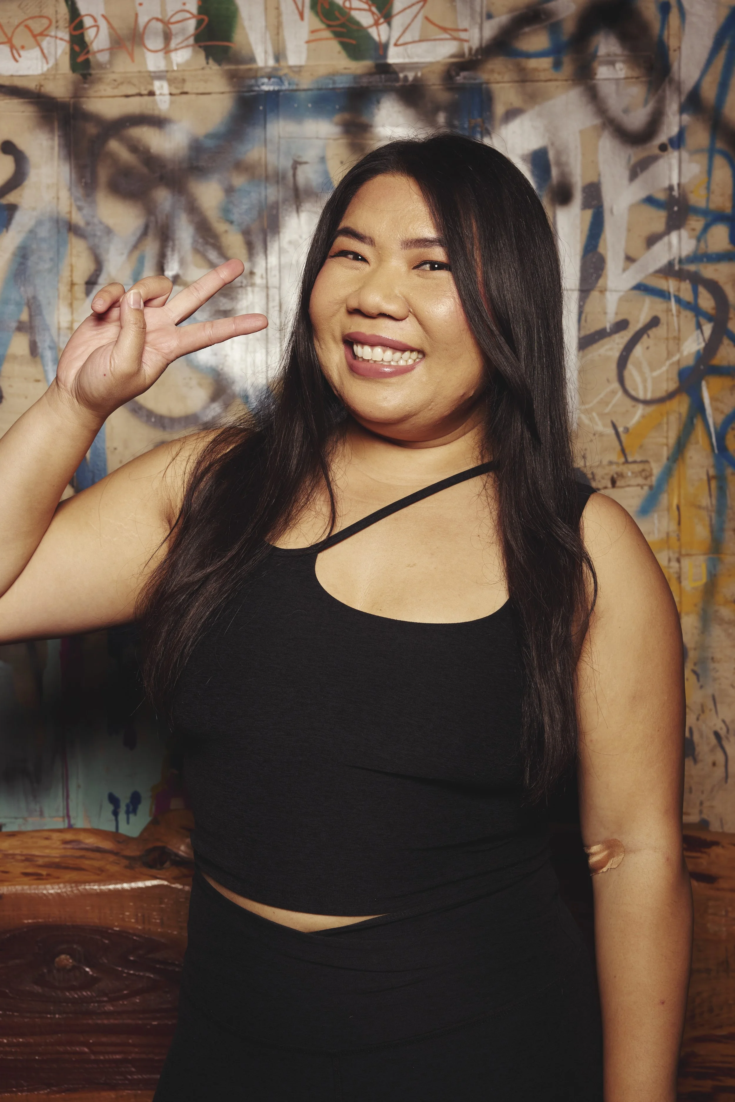 Black and white portrait of a smiling woman outdoors with blurred trees in the background, wearing a headband and necklace.