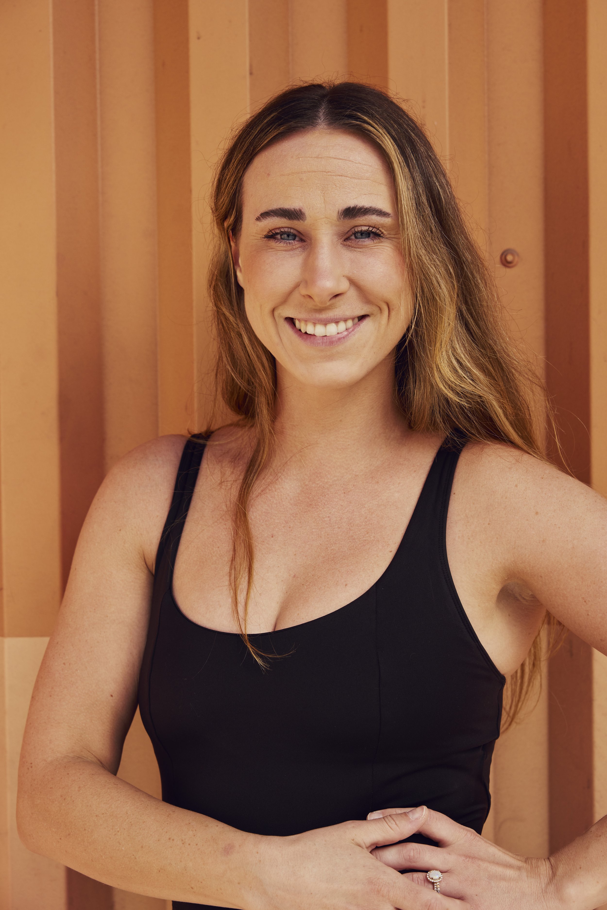 A woman with red hair smiling and posing against an orange wooden background, wearing a leopard print top.
