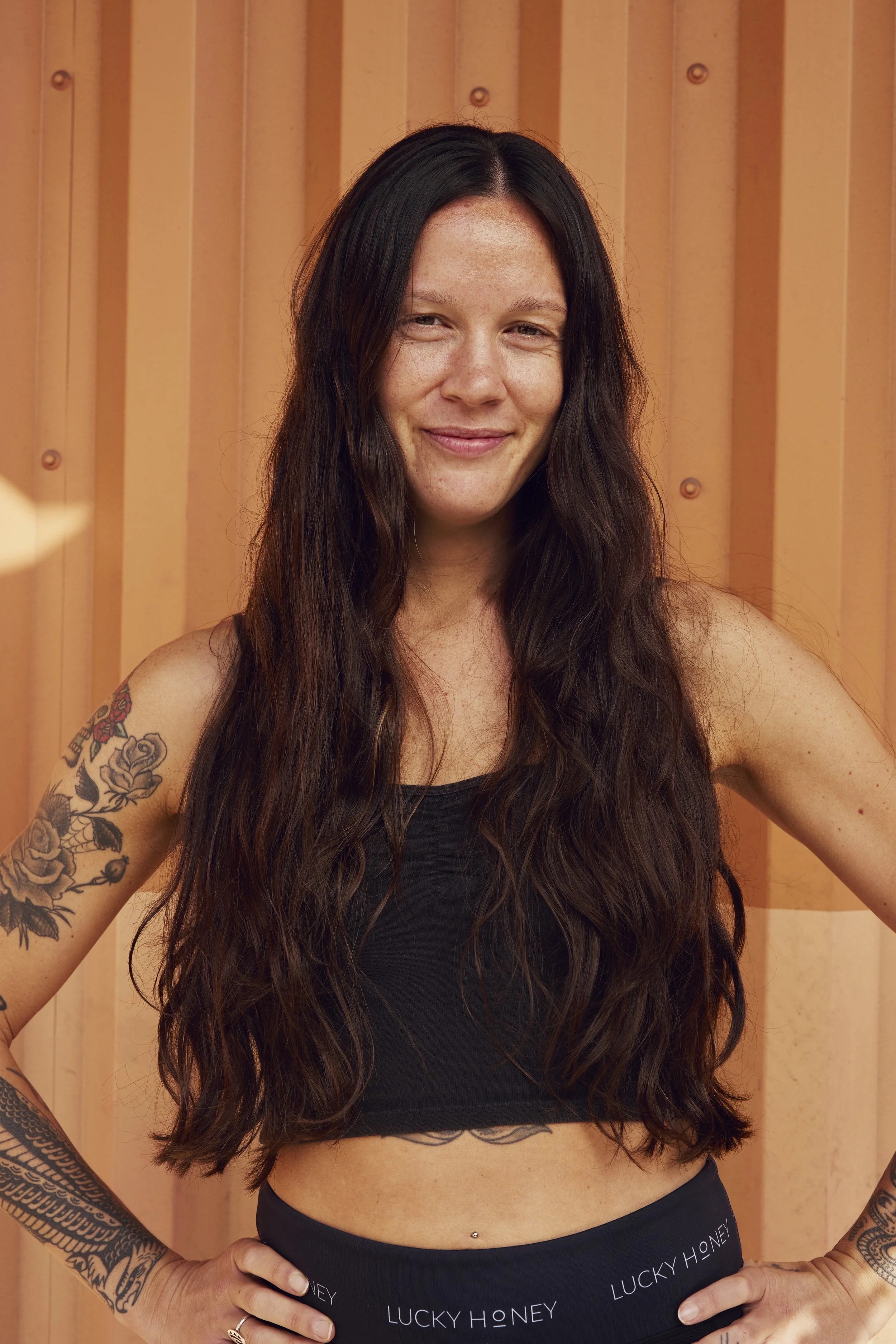 Woman with long braided hair, tattoos on arms and chest, wearing a black tank top, with hands pressed together in prayer, looking upward.
