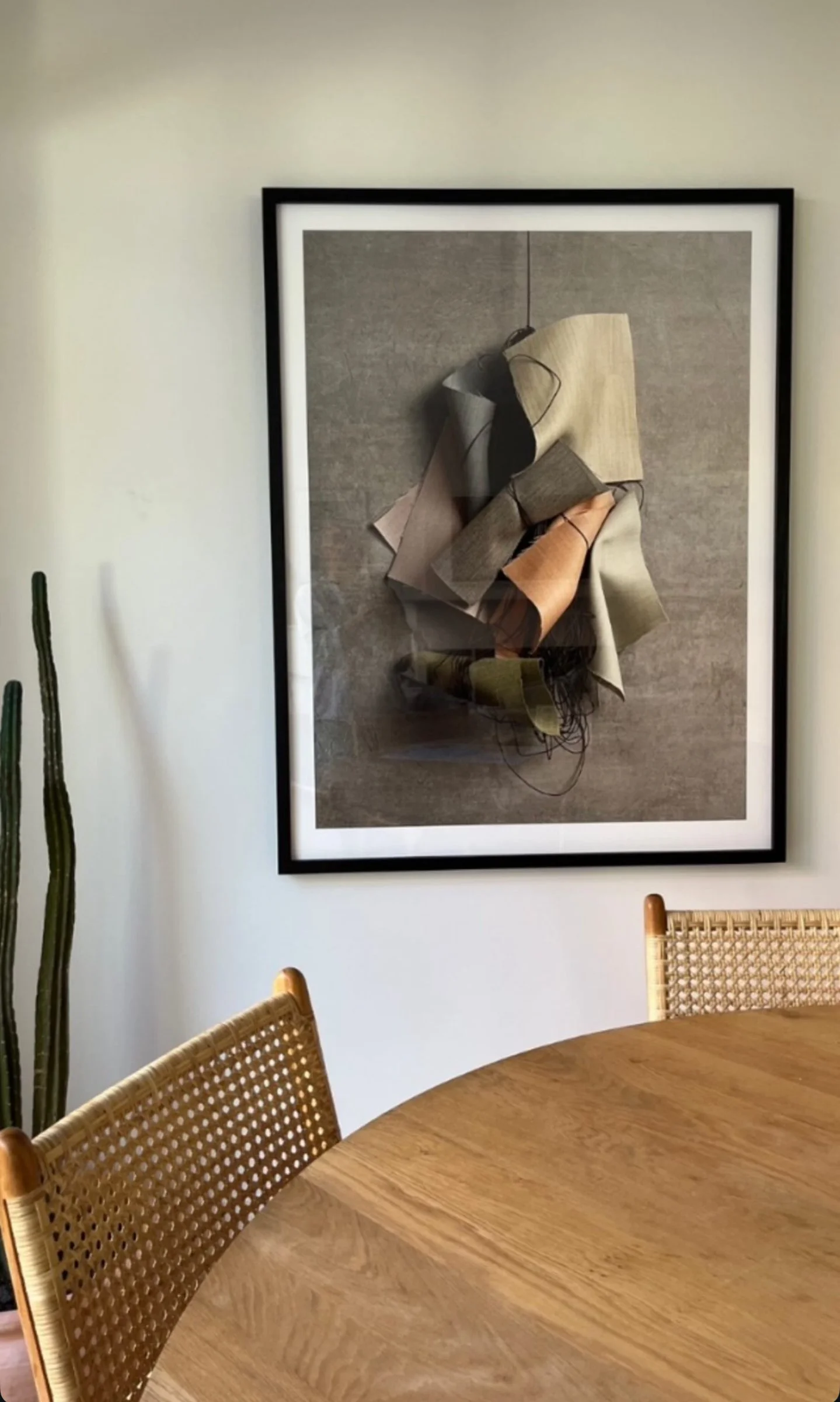 Decorative art piece featuring layered fabric swatches hanging on a gray background, displayed in a black frame.
