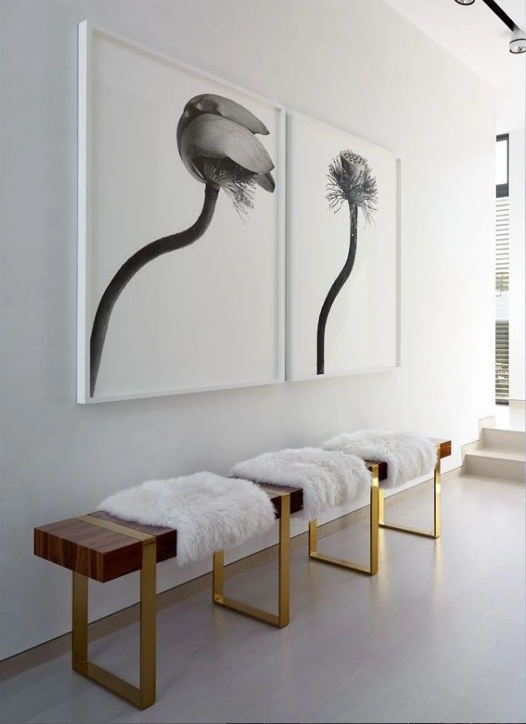 Minimalist interior with three white fur-covered benches with gold metal frames, white wall with black-and-white floral artwork, and a window with vertical blinds.