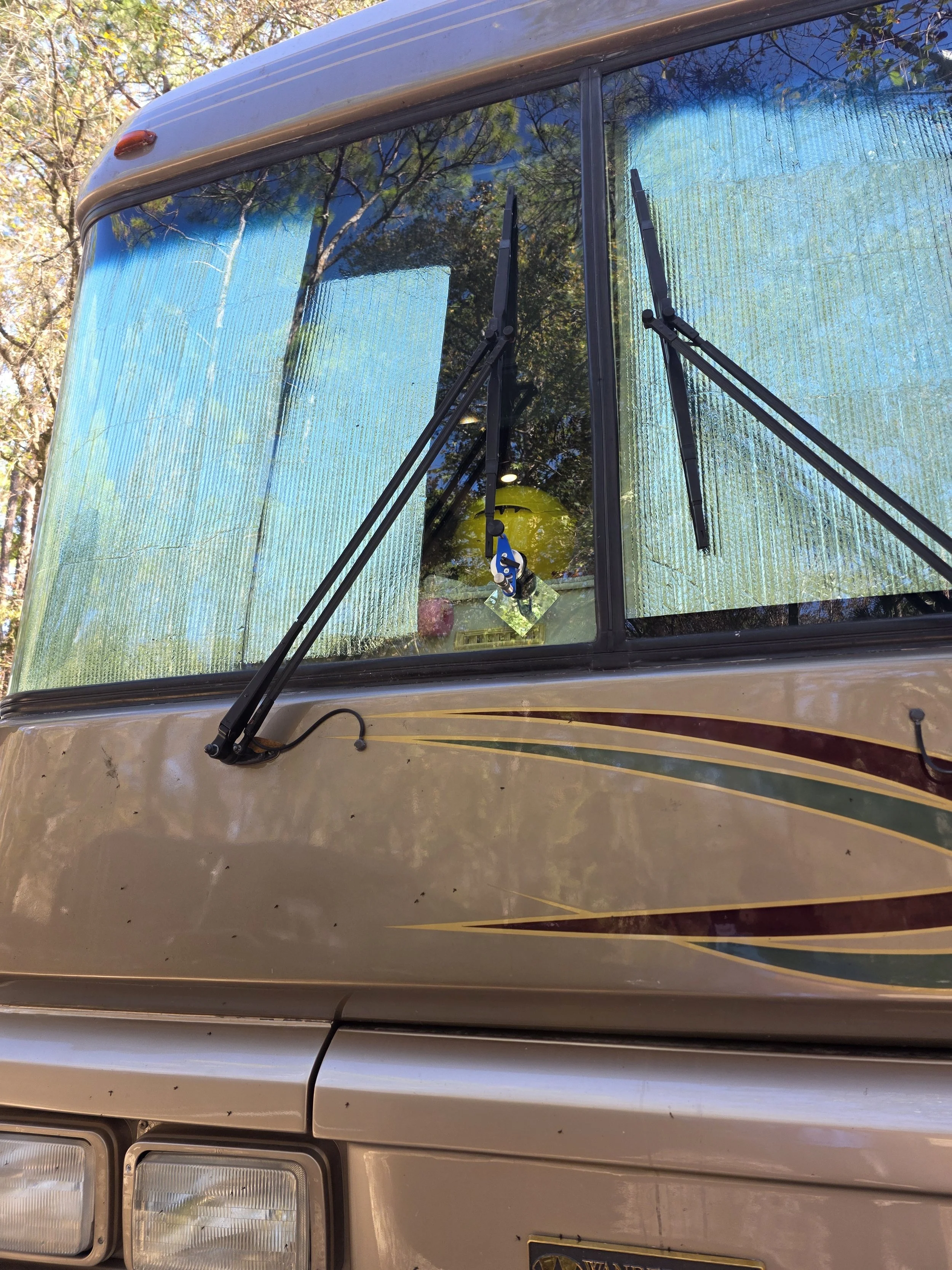 Front of a beige motorhome or RV with large blue-tinted windshield, black windshield wipers, and a decorative stripe pattern.