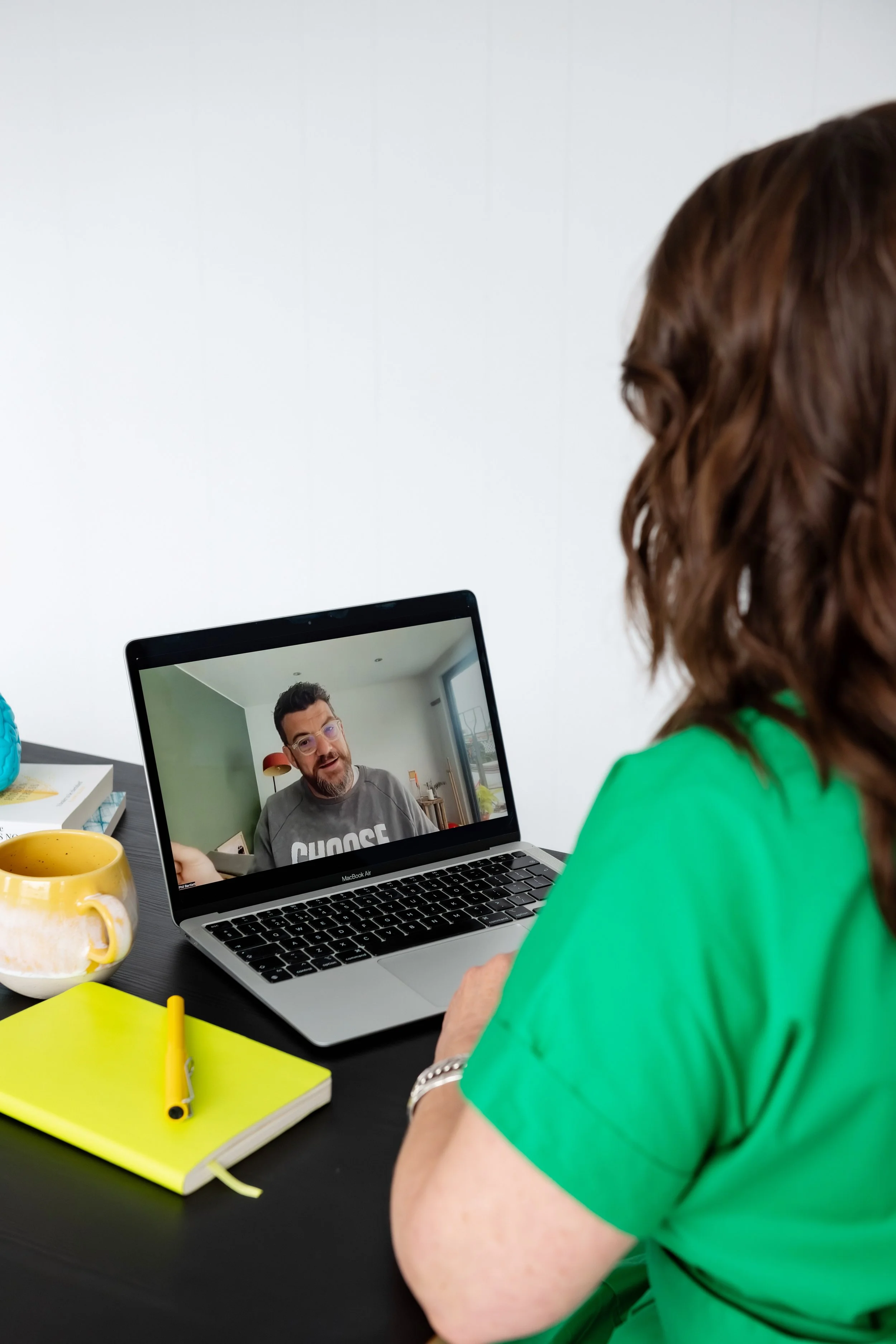 Sarah Bellorini, Leadership Identity Coach for Gen X, sitting at a desk using a laptop for a video call with a man wearing glasses on the screen.
