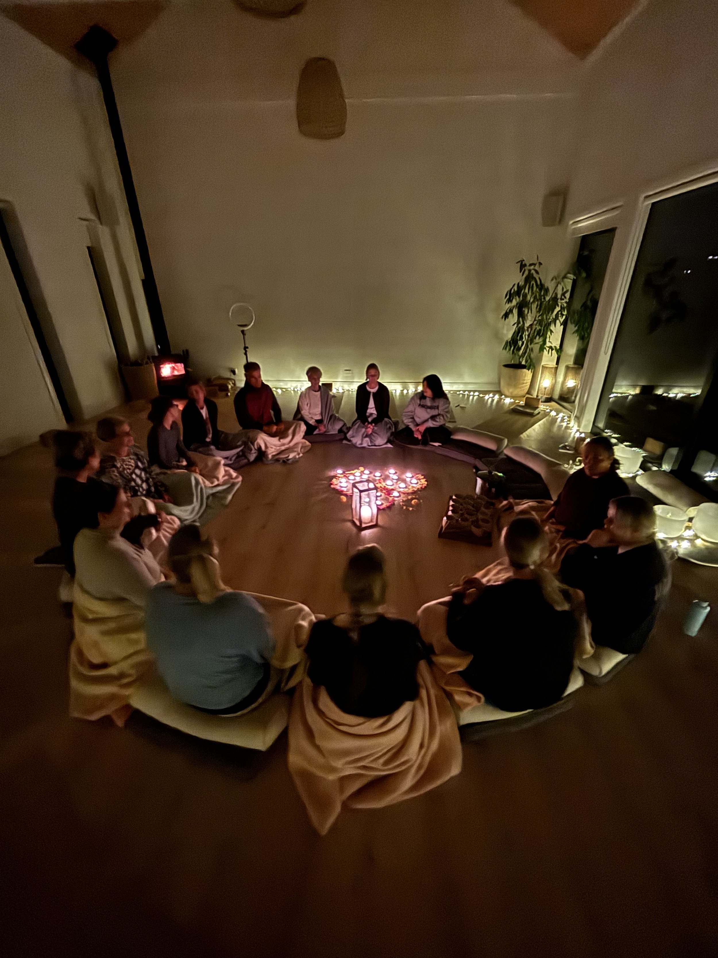 A group of people in a welcome circle on the floor, with candles in the center, at the Winter Wellness Yoga retreat for busy corporate women