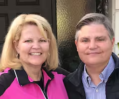 A woman and a man standing outdoors, smiling at the camera.