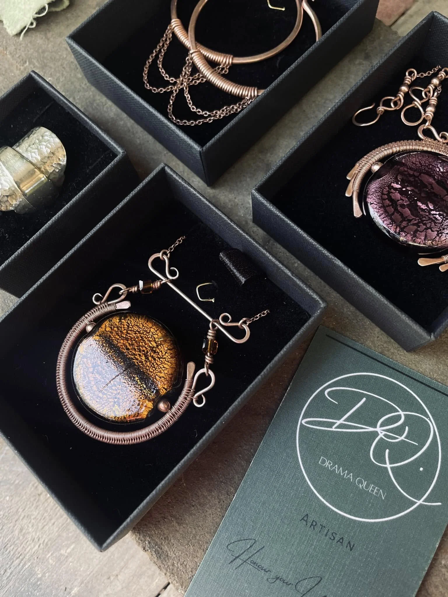 Collection of jewelry including necklaces, earrings, and bracelets in black boxes with an artisan label.