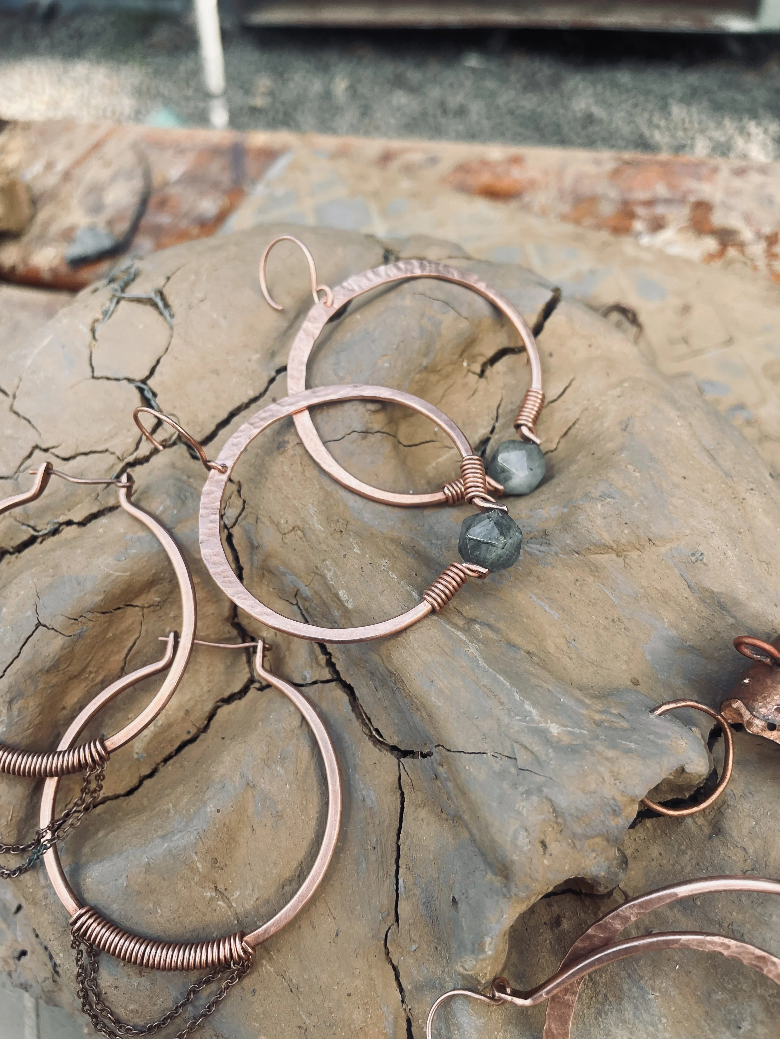 copper hoop earrings with labradorite beads, displayed on a cracked beige stone surface.