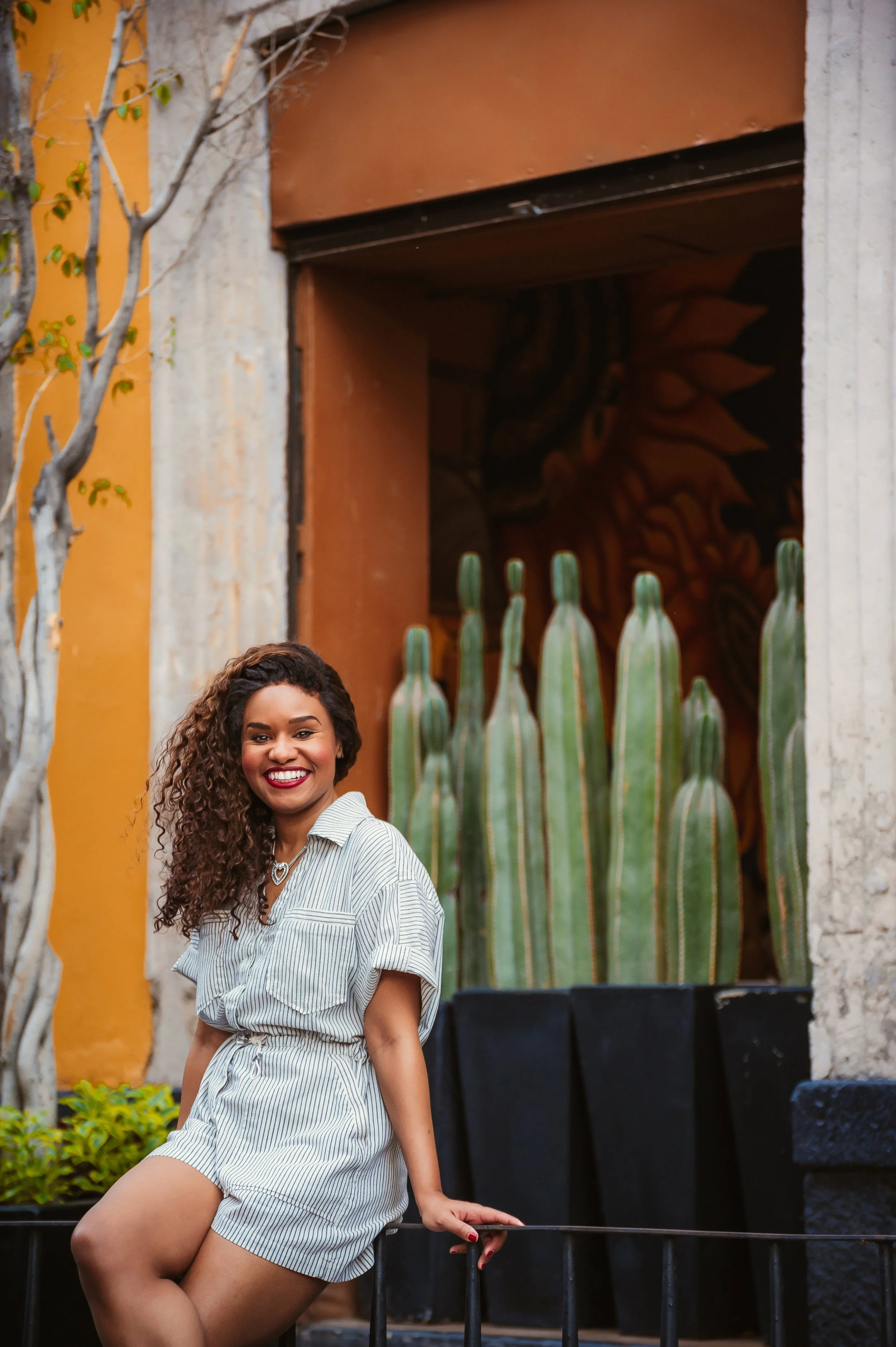 A woman in a striped dress smiling sitting outdoors near a cactus and colorful mural.