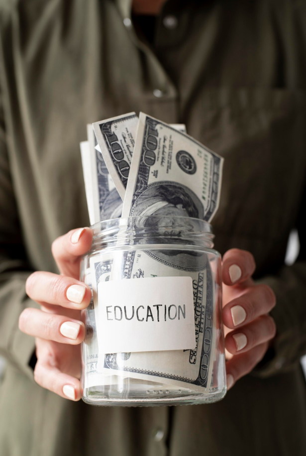 Person holding a glass jar labeled 'Education' filled with U.S. dollar bills.