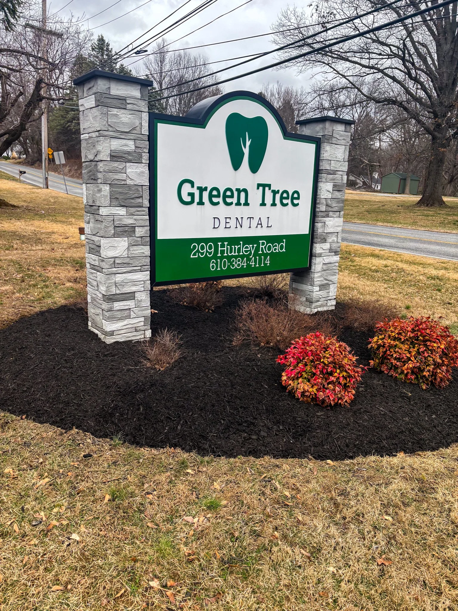 Sign for Green Tree Dental on Hurley Road, surrounded by mulch and bushes, with trees and power lines in the background.