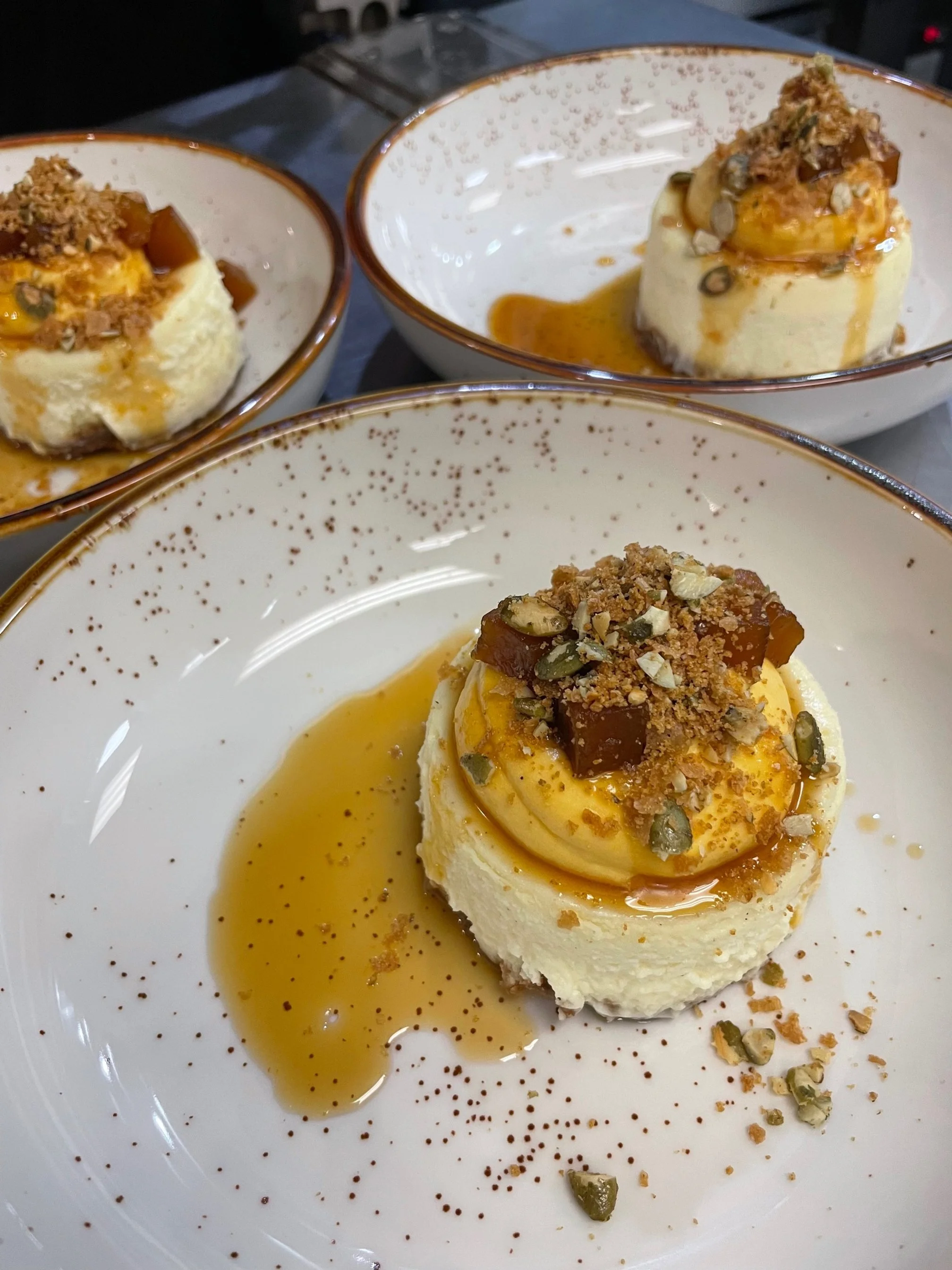 Three bowls of individual cheesecakes topped with chopped nuts and caramel sauce.