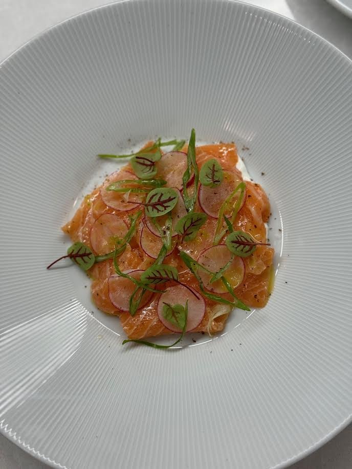 Salmon sashimi topped with radish slices and microgreens in a white bowl.