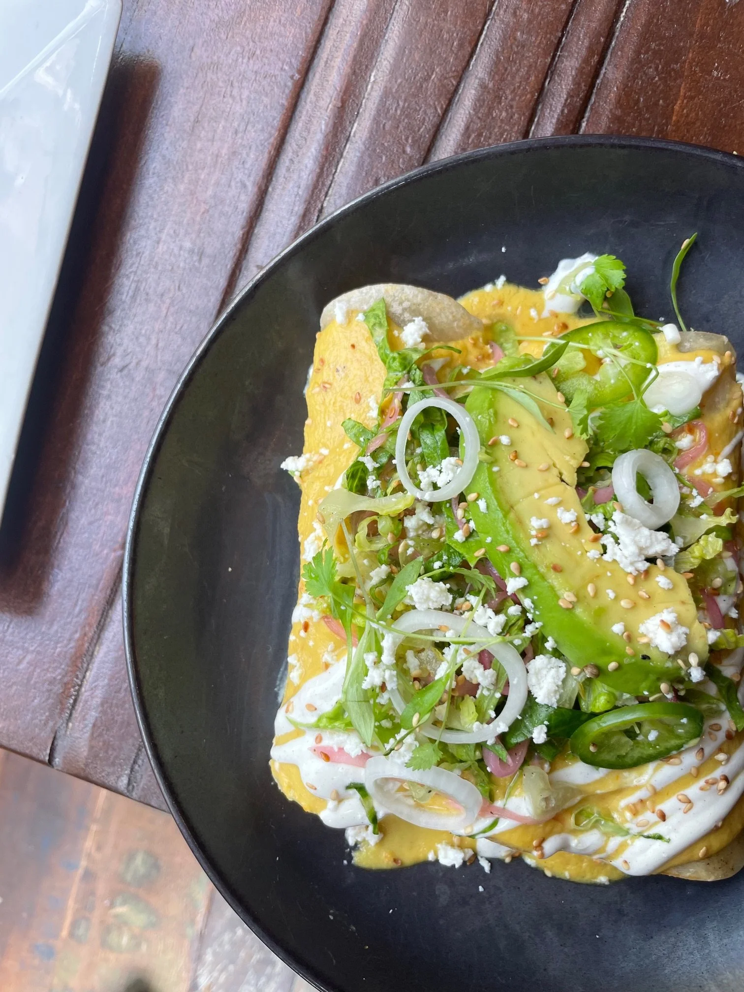 Tostada with avocado, cilantro, onions, cheese, and sauce on a black plate.