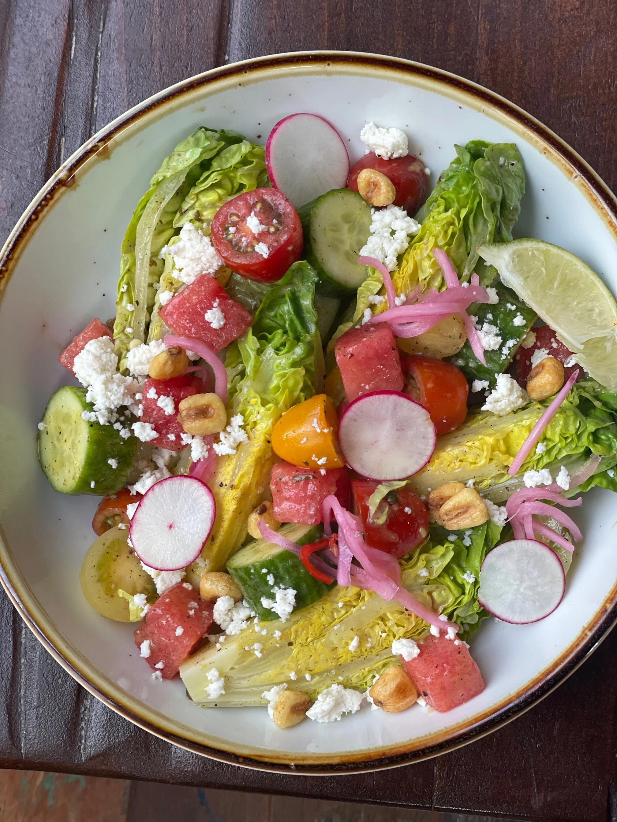 Fresh vegetable salad with cherry tomatoes, radishes, cucumber, watermelon, pickled onions, crumbled cheese, and chopped nuts served in a white bowl