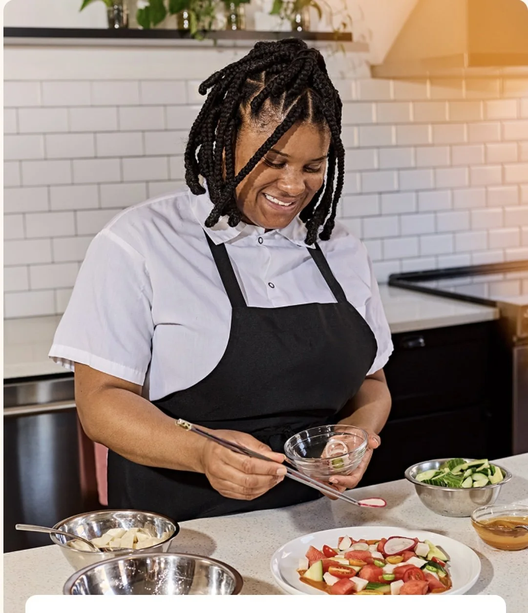 Chef Taj holding a pair of kitchen tweezers in the right hand and a small glass bowl in her left garnishing a salad with a slice of radish.