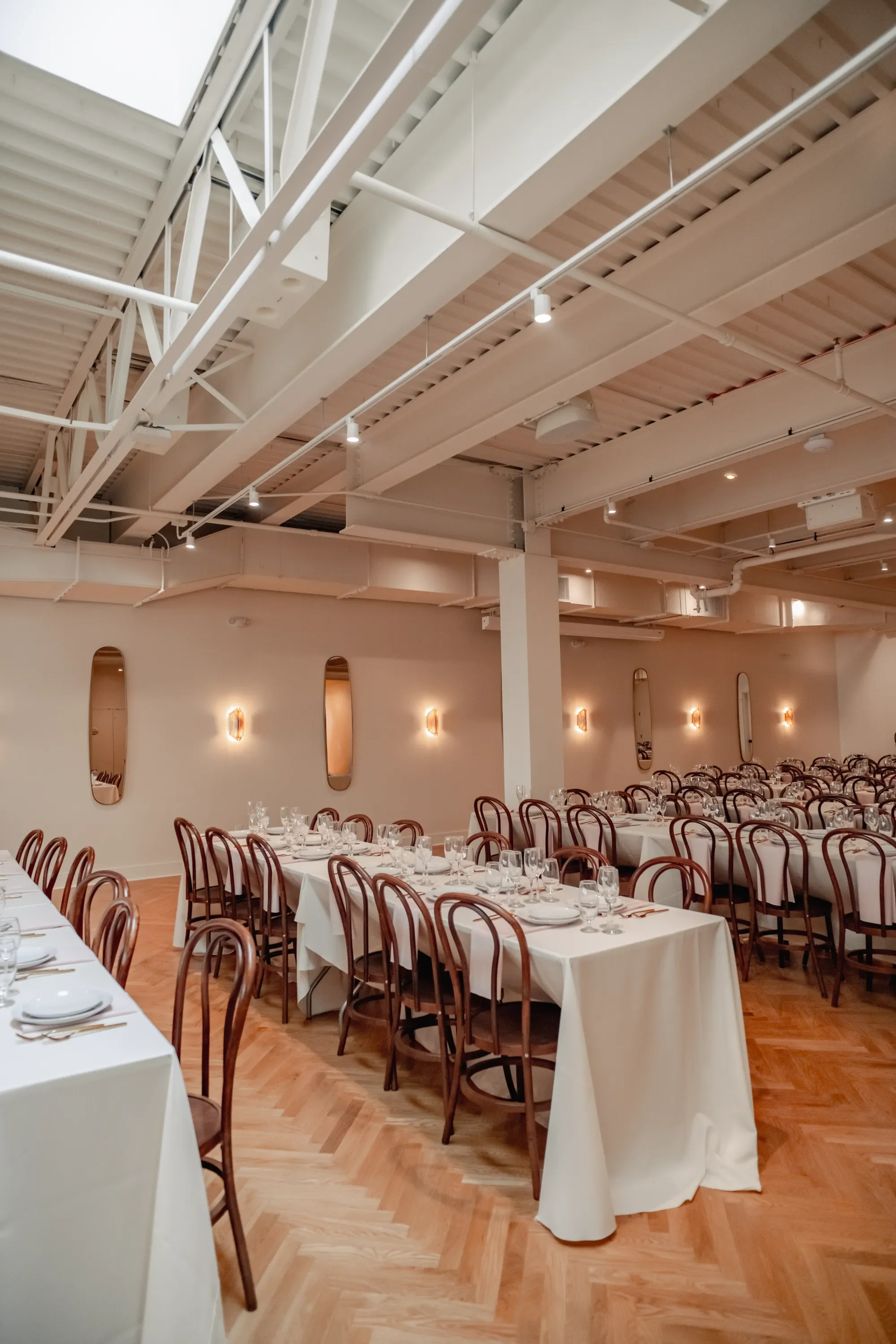 Elegant dining setup with long tables covered in white tablecloths, set with plates, glasses, and silverware, in a modern, well-lit banquet hall.