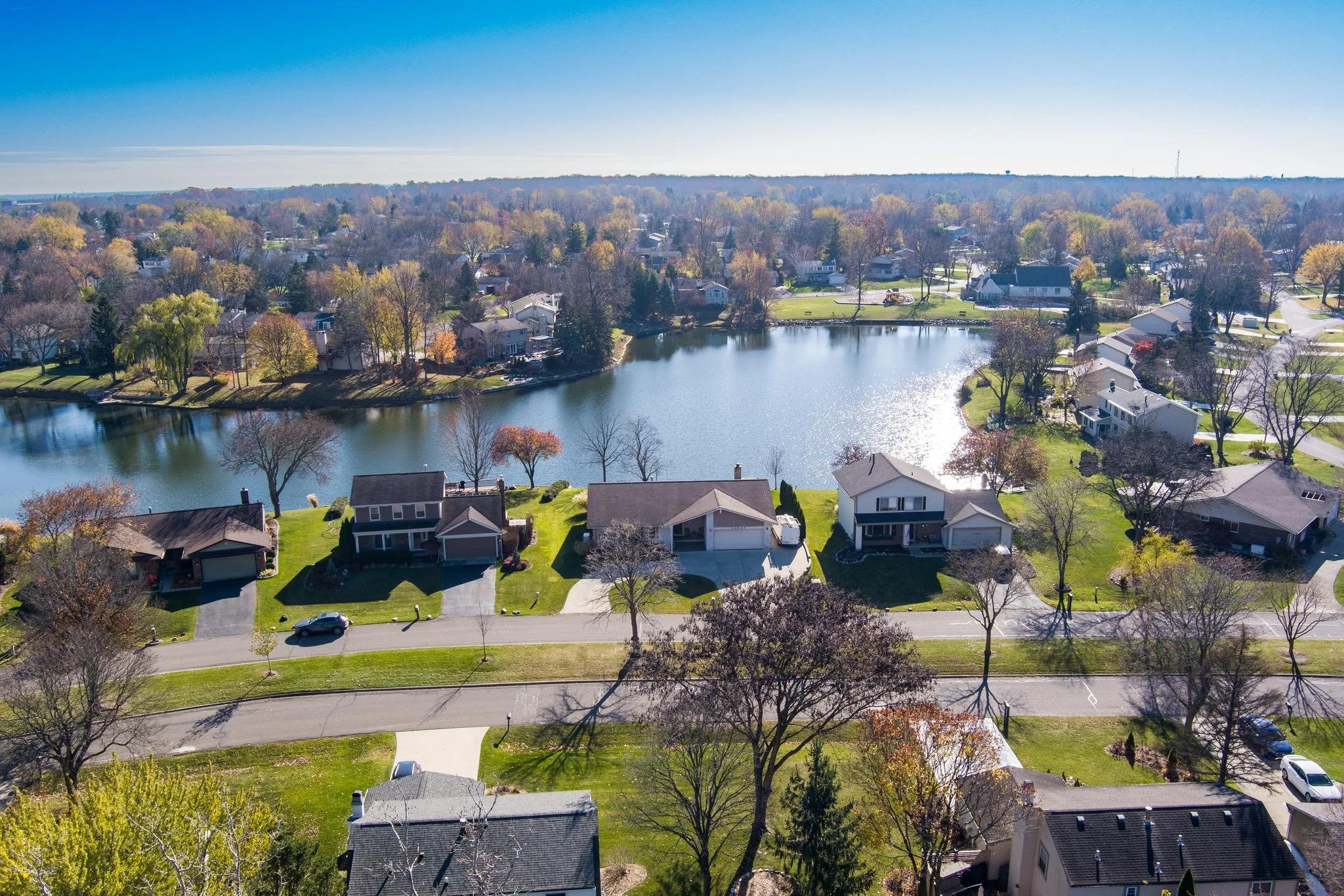 Aerial view of a suburban neighborhood with houses, trees, and a central lake on a sunny day.
