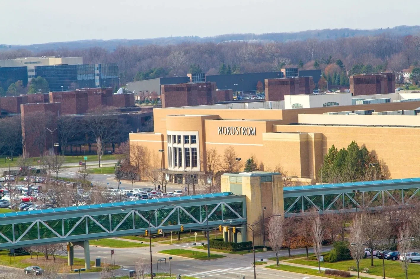 An outdoor view of a shopping mall with a large Nordstrom store, parking lot, trees, and a skybridge.