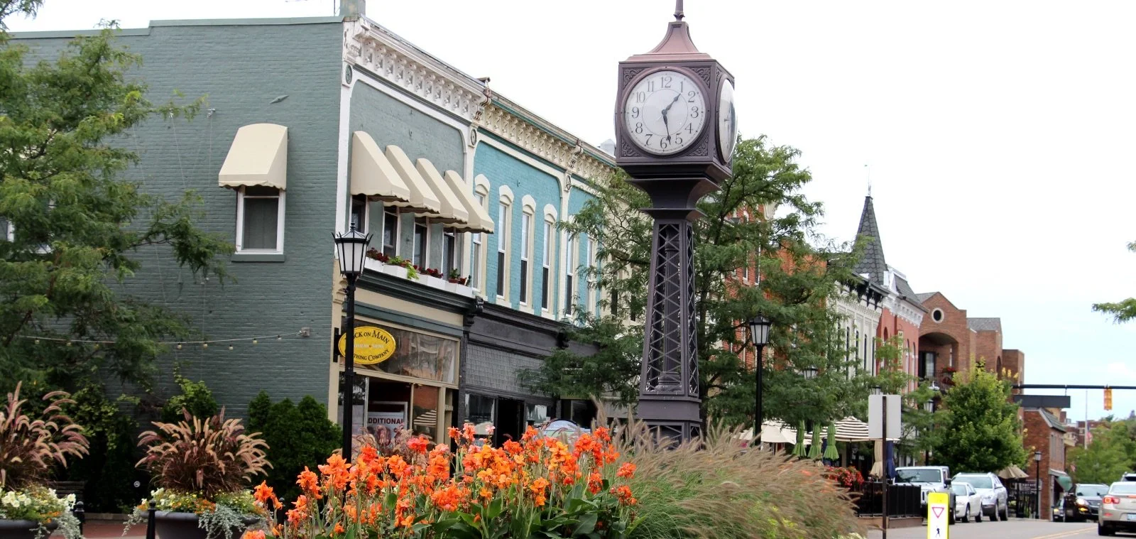 A street scene with a vintage-style clock tower, colorful historic buildings, and flower beds in the foreground.