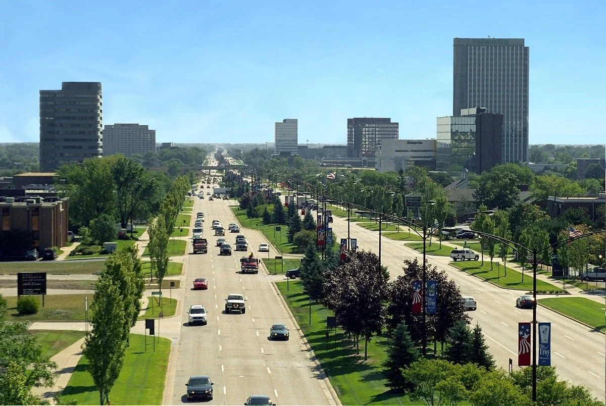City street with cars, trees, and buildings in the background on a sunny day.