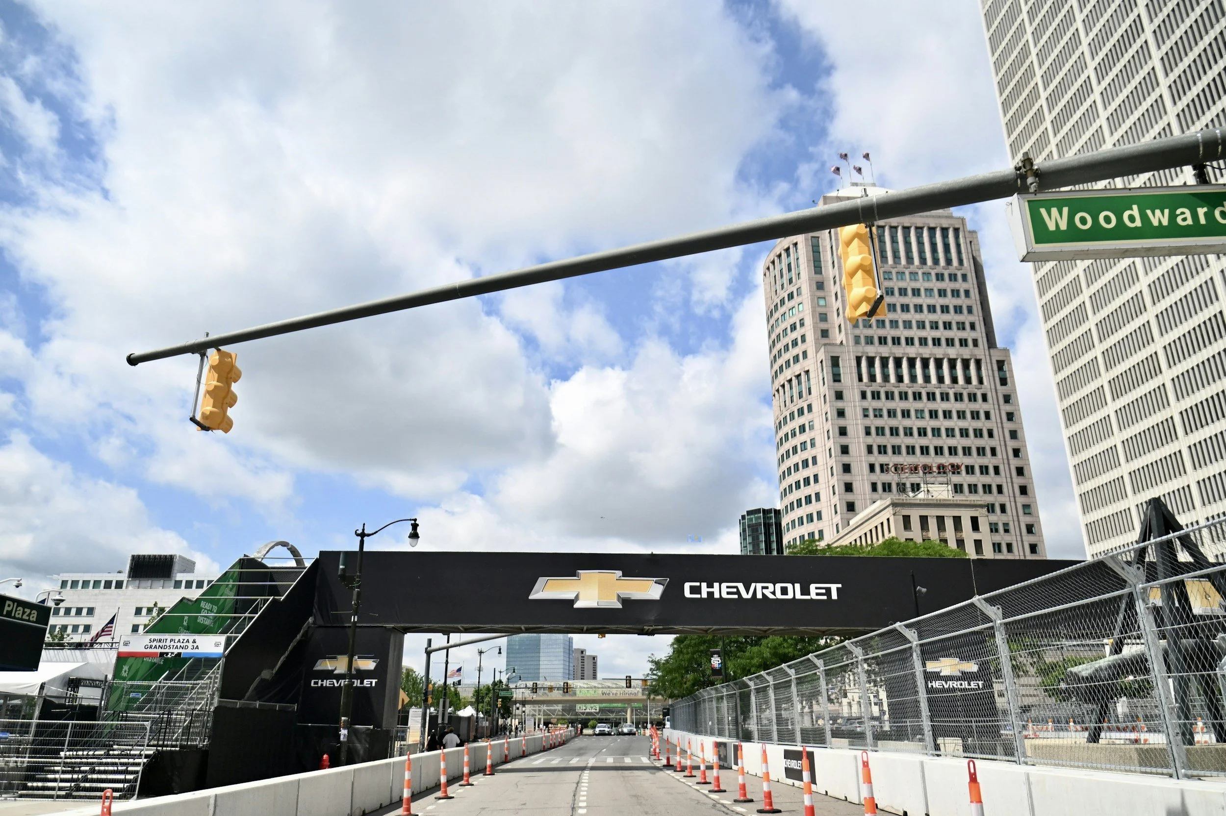 City street scene with tall buildings, traffic lights, and a Chevrolet advertisement archway over the street, with construction barriers and fencing along the sidewalk.
