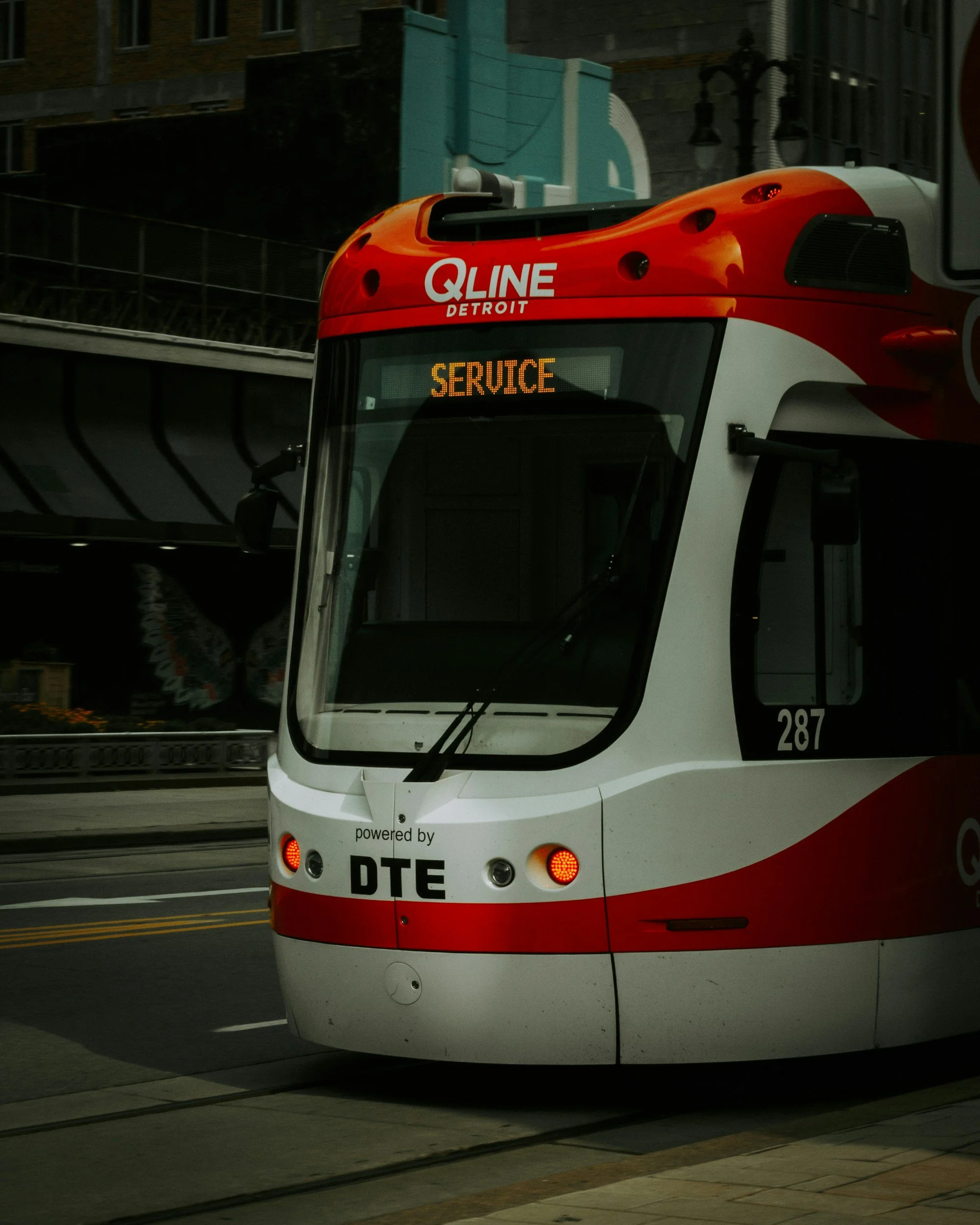 Front of a modern red and white public transit tram with an electronic display reading 'SERVICE' and the logo 'Q LINE DETROIT'.