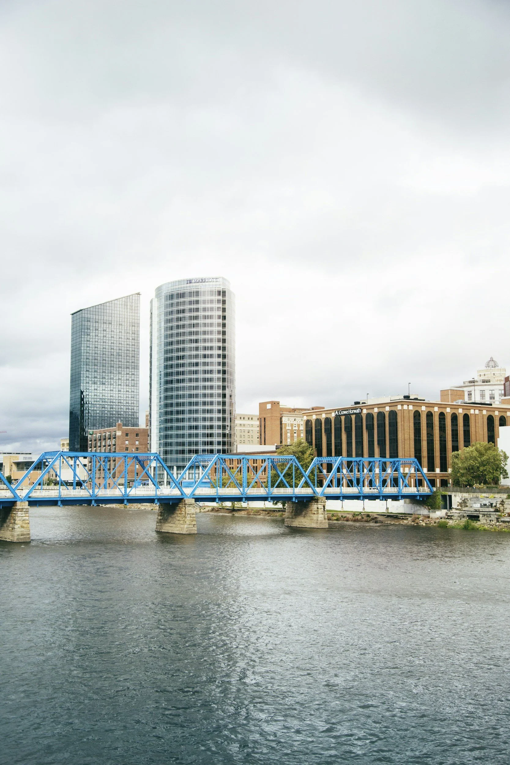 City skyline with modern glass buildings and a blue bridge over a river in the foreground.