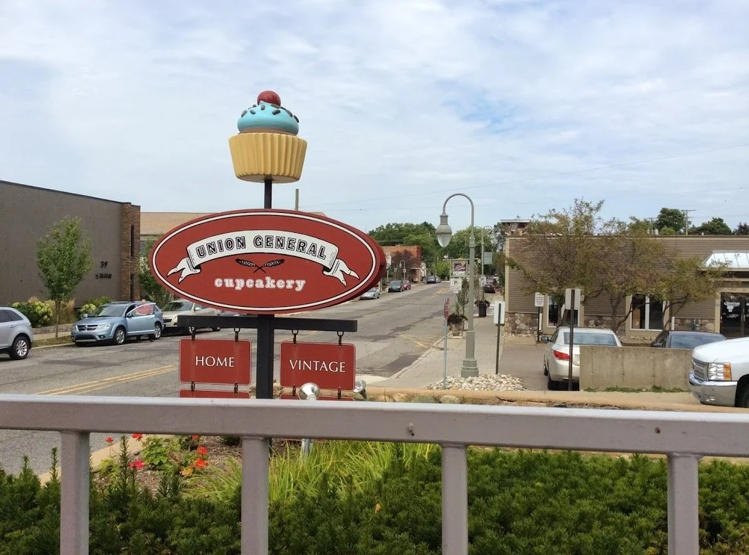Sign for Union General cupcake shop with photo of a cupcake with blue frosting and cherry on top, on a lamppost in a small town.