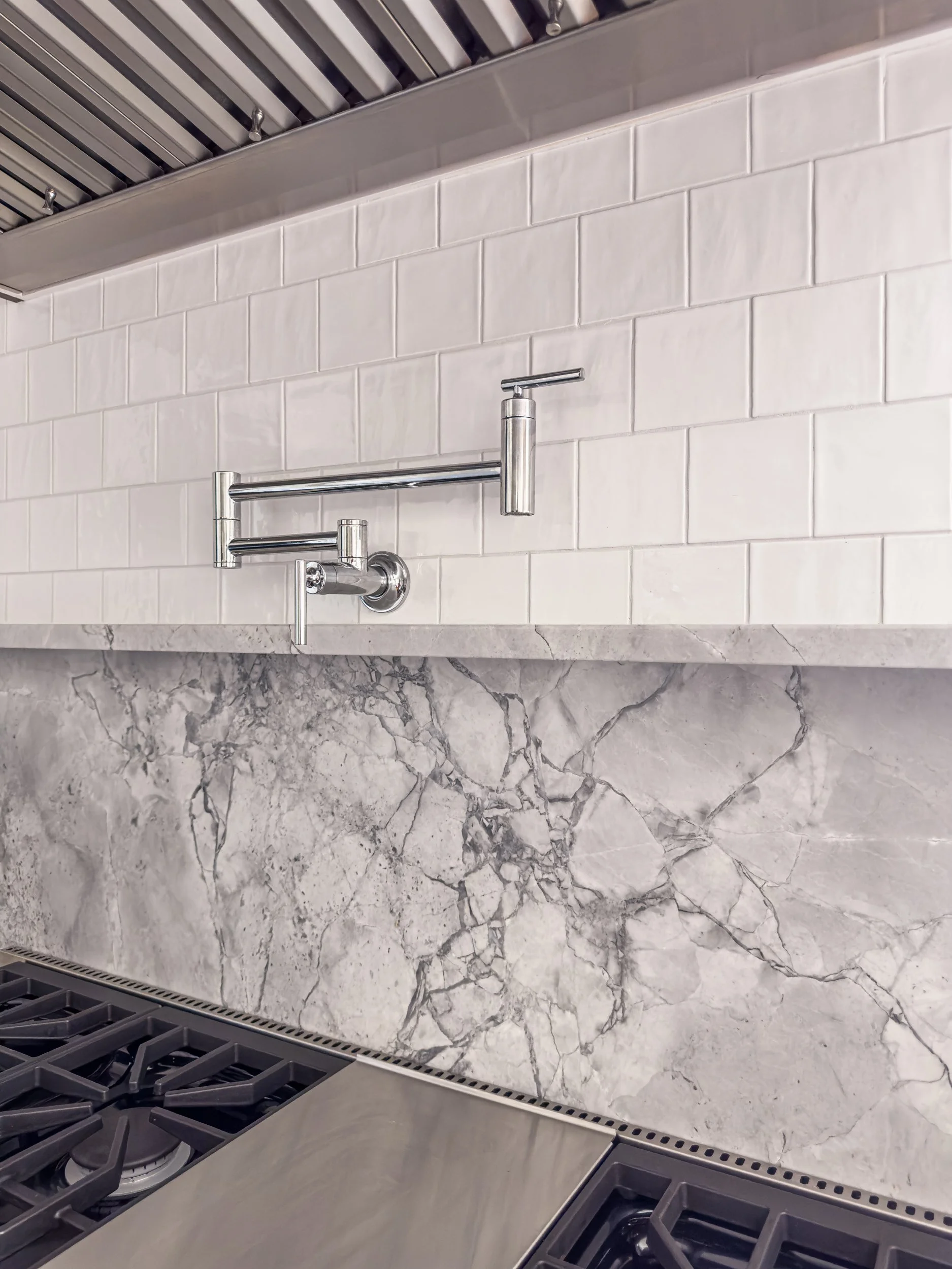 Best general contractor, home builder, and home remodeler on the Northshore in Andover, Massachusetts (MA), developed this modern kitchen with a marble countertop, a white tiled backsplash, and a stainless steel ventilation hood.