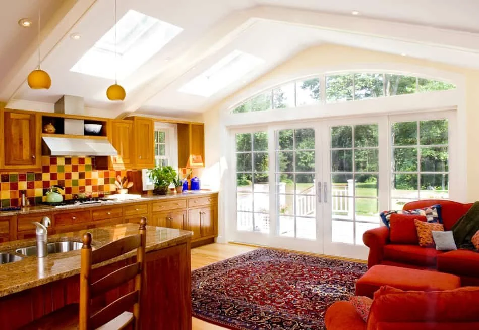 Bright kitchen and living area with large sliding glass doors, wooden cabinets, colorful backsplash, and red furniture.