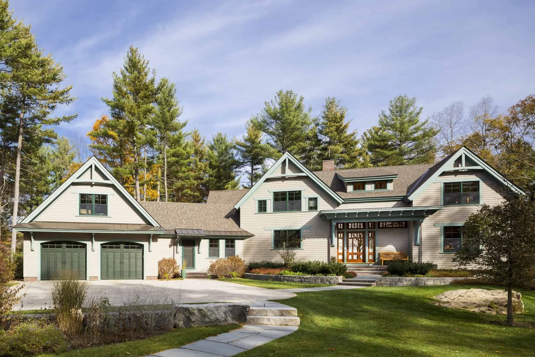 A large house with a gray exterior, green doors, and multiple gabled roofs, surrounded by trees and a landscaped yard.