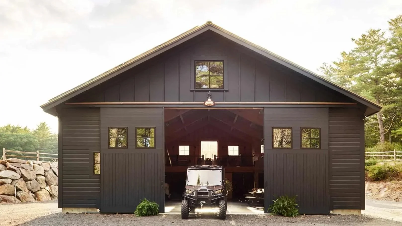 A large custom modern black multi-functional party barn with open sliding double doors, a small window above, and four windows on each side. Inside, there is a loft with additional windows and racks. 