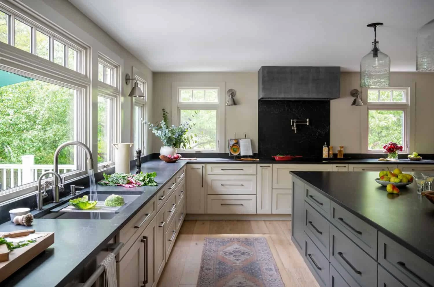 Modern kitchen with black countertops, white cabinets, large windows with green view, and kitchen island.