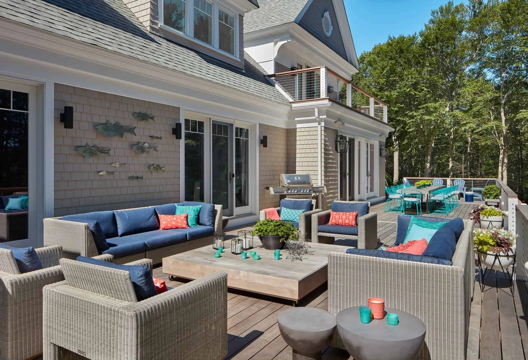 Outdoor deck with wicker furniture, cushions, pillows, a coffee table, a grill, and string lights, surrounded by trees.