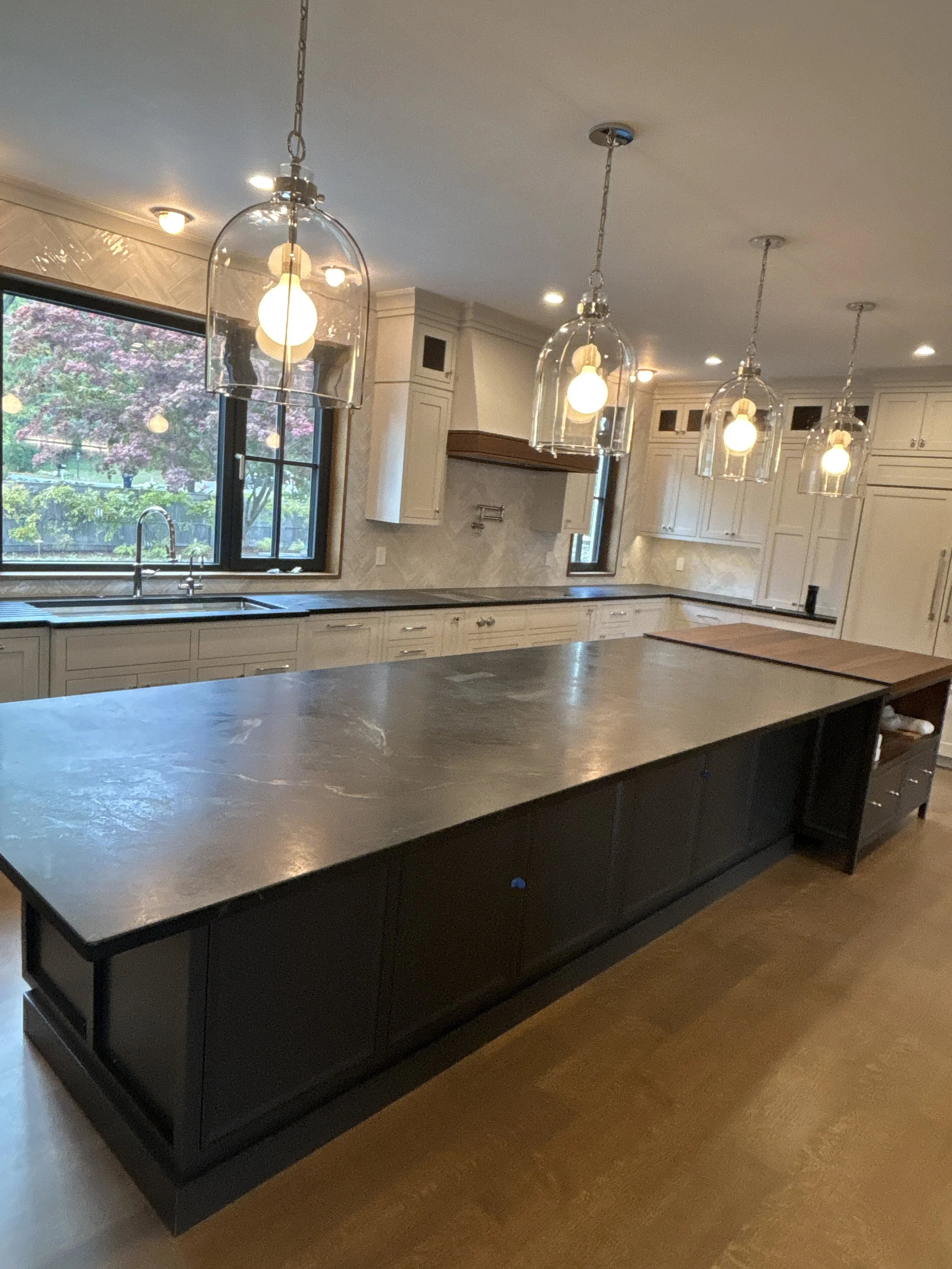 Best general contractor, home builder, and home remodeler on the Northshore in Andover, Massachusetts (MA), developed this modern kitchen with a large dark island in the foreground, white cabinetry in the background, and pendant lights.
